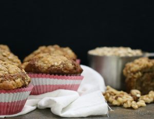 3 Healthy Banana Nut Muffins with Pink & White Paper Wrappers on Countertop with Measuring Cup of Oats #recipe | Vitacost.com/blog