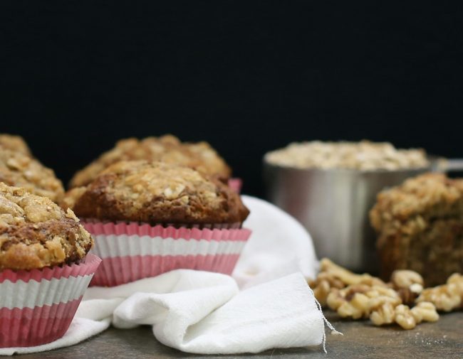 Healthy Banana Nut Muffins to Go 3 Healthy Banana Nut Muffins with Pink & White Paper Wrappers on Countertop with Measuring Cup of Oats #recipe | Vitacost.com/blog