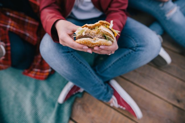Teens with Junk Food Addiction Sit on Boardwalk with Burger in Hands, Hurting Their Health | Vitacost.com/blog