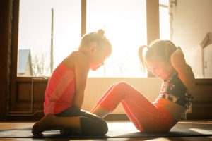 Two Young Girls Helping Each Other Exercise Inside During the Winter | Vitacost.com/Blog