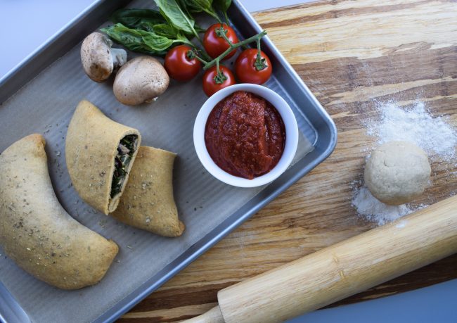Calzone Recipe with Vegan Pesto  2 Calzone Pizza Pockets on Baking Sheet with Recipe Ingredient & Marinara Dipping Sauce | Vitacost.com/blog
