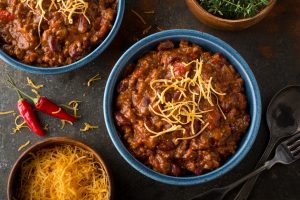 Slow Cooker Chipotle Turkey Chili with Shredded Cheese in Blue Bowl on Countertop #recipe | Vitacost.com/blog