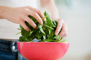 Hands Tossing Spinach Leaves in Red Bowl to Maintain pH Balance on Alkaline Diet | Vitacost.com/blog