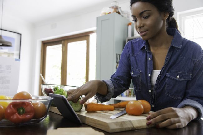 Woman at Kitchen Table on Tablet Goes Over Her Heart Healthy Diet Meal Plan | Vitacost.com/blog