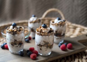 4 Glasses on a Wood Cutting Board, Filled with a Vegan Parfait Recipe & Topped with Fruit, Whipped Coconut Cream | Vitacost.com/blog