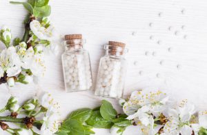 Two Bottles of Homeopathic Remedies for Pain Relief on White Table With Flowers | Vitacost.com/blog
