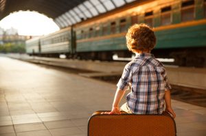 Child Following Travel Tips for Kids With Autism Sitting on Suitcase at Train Station | Vitacost.com/blog