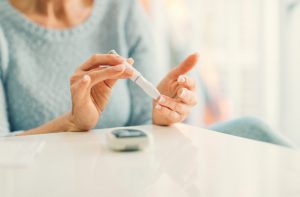 Woman Aware of Diabetes Facts Testing Her Blood Sugar Levels While Sitting at a Table | Vitacost.com/blog