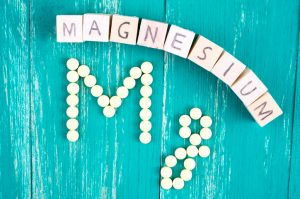 Block letters and Supplement Capsules Spelling Magnesium on Teal Wooden Table | Vitacost.com/blog
