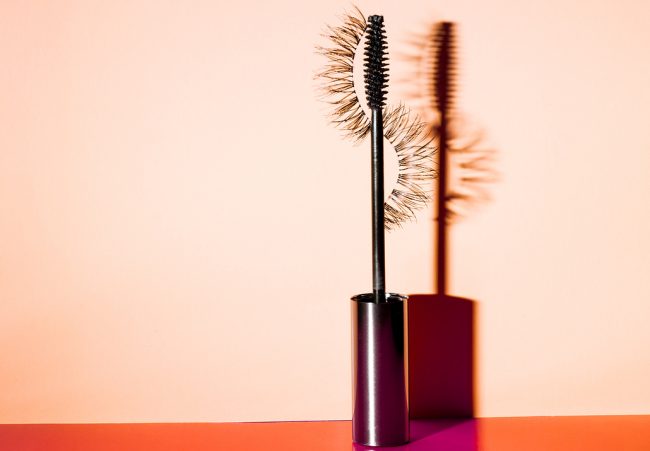 Mascara Wand and Its Shadow on Orange Table Representing How to Grow Longer Eyelashes | Vitacost.com/blog