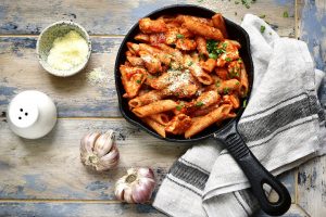 Cast Iron Skillet on Wood Table with Buffalo Chicken Penne Pasta, Plus Garlic Cloves #recipe | Vitacost.com/blog