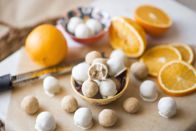 Bowl of Orange Creamsicle Truffles on Parchment Paper with Sliced Oranges #recipe | Vitacost.com/blog
