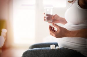 Side View of Torso of Pregnant Woman in White Shirt Taking Prenatal Supplements | Vitacost.com/blog
