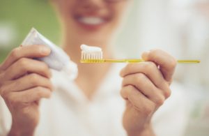 Smiling Woman Holding Yellow Toothbrush Trying Different Types of Toothpaste | Vitacost.com/blog
