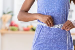 Woman Concerned About the Effects of Obesity on Health Measuring her Wasitline | Vitacost.com/blog