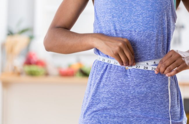 Woman Concerned About the Effects of Obesity on Health Measuring her Wasitline | Vitacost.com/blog