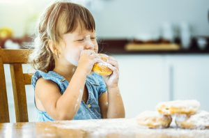 Little Girl Enjoying One of the Unhealthiest Foods for Kids Biting into Powdered Sugar-Covered Donut | Vitacost.com/blog