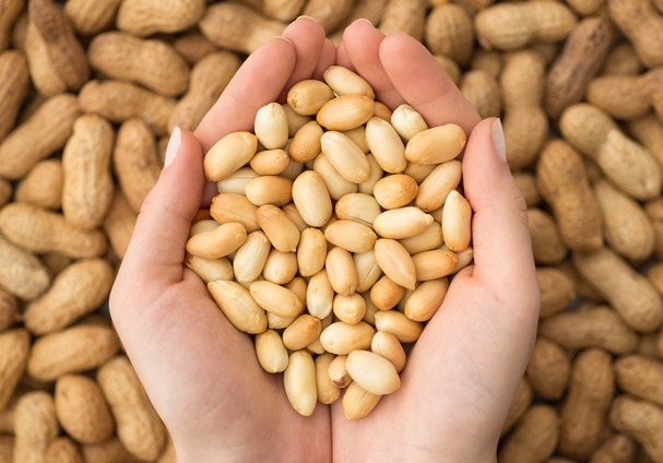 Woman Without Food Allergies Holding Handful of Shelled Peanuts Over Pile of Unshelled Peanuts | Vitacost.com/blog