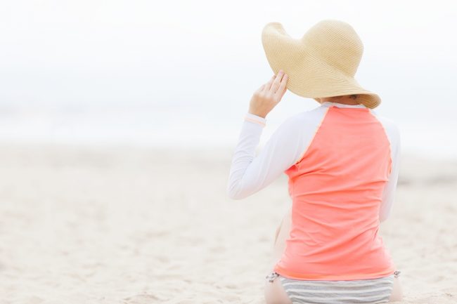 Woman on Beach With Hat & Long Sleeves is Worried About Severe Types of Sunburn & How to Treat Sunburn | Vitacost.com/blog