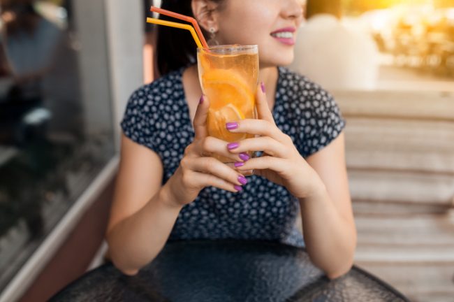 Woman Trying to Quit Drinking Soda Drinking Glass of Orange Flavored Water While Sitting on Steps | Vitacost.com/blog
