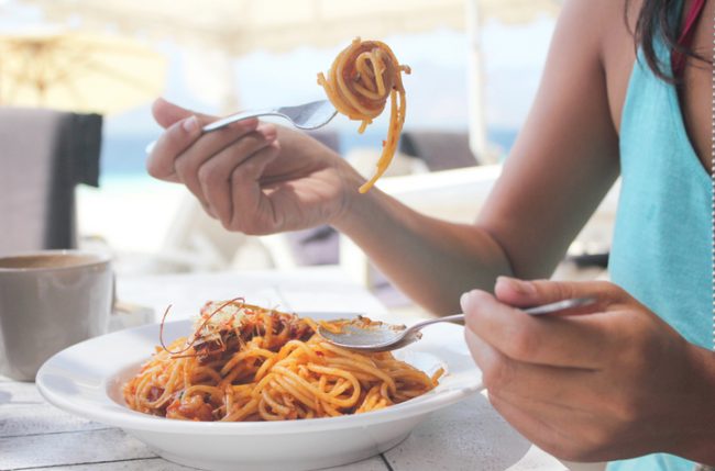 Woman at Restaurant Twirling Pasta on Fork Wondering to Herself: "Is Pasta Healthy?" | Vitacost.com/blog