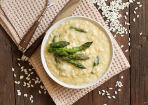 Bowl of Asparagus Risotto on Wooden Table Surrounded by Rice | Vitacost Blog