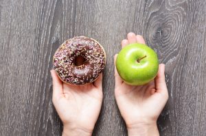 Pair of Hands Holding Apple and Donut to Represent the Difficulty in Deciding to Eat Healthier | Vitacost.com/blog