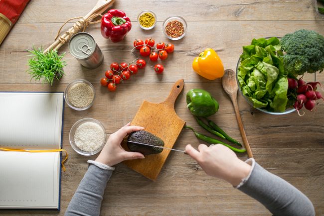 Person Cutting Avocado and Other Veggies on Cutting Board to Prepare Vegan Meal | Vitacost.com/Blog