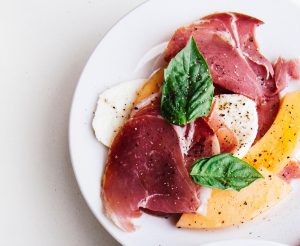 Seasoned Prosciutto and Melon Slices With Mozzarella and Basil on White Plate #recipe | Vitacost.com/blog