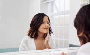 Middle-Aged Woman Checking for Under Eye Issues in Bathroom Mirror | Vitacost.com/blog