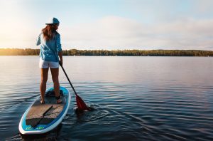 Back View of Woman in Baseball Cap Trying Stand-Up Paddleboarding (SUP) on Serene Lake at Sunset | Vitacost.com/blog
