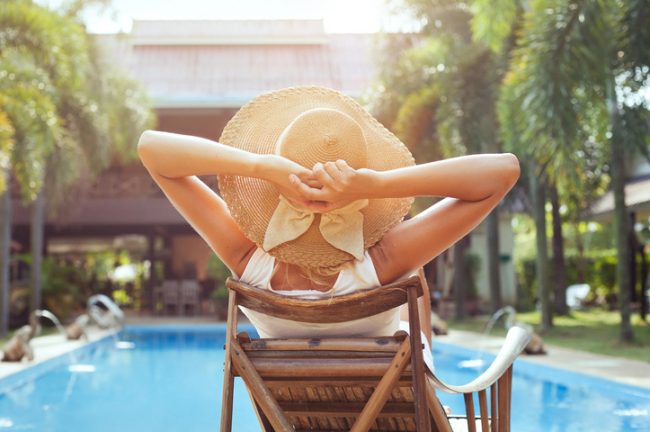 Back View of Woman in Sun Hat Relaxing Poolside While Practicing Natural Skin Care Tips for Summer | Vitacost.com/blog