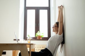Woman Practicing Mindfulness Stretching Arms While Sitting at Table With Laptop Computer | Vitacost.com/blog
