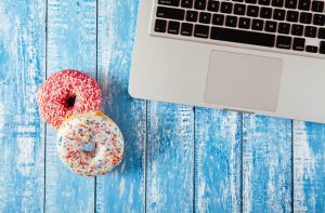 Sprinkled Donuts Beside Laptop Computer on Blue Table to Represent Concept of Not Eating Healthier at Work | Vitacost.com/blog
