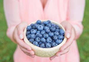Woman in Pink Dress Holding Woven Bowl Filled With Blueberries as Part of Her Acne Diet | Vitacost.com/blog