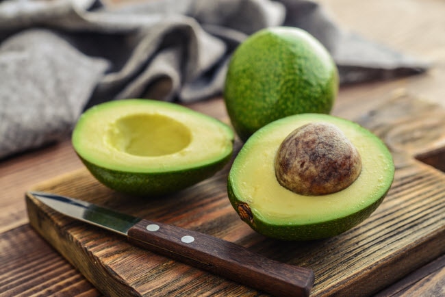 Avocado Nutrition Represented by Freshly Cut Avocado with Knife on Wooden Cutting Board | Vitacost.com/blog