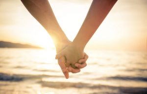 Stages of the Grieving Process Represented by Couple Holding Hands at Sunset in Front of Ocean | Vitacost.com/blog