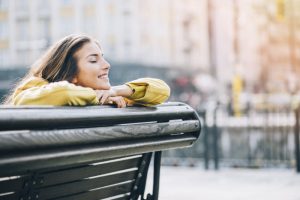 Content-Looking Woman in Yellow Jacket Exercising Positive Self Talk on City Park Bench | Vitacost.com/blog