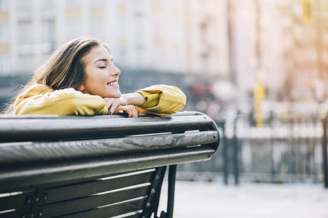 Content-Looking Woman in Yellow Jacket Exercising Positive Self Talk on City Park Bench | Vitacost.com/blog