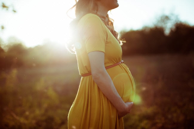 Woman Following Advice on How to Have a Healthy Pregnancy Standing in Field Holding Belly | Vitacost.com/blog