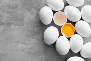 Scattered Eggs Including One Cracked Open on Gray Surface Representing Importance of Salmonella Prevention | Vitacost.com/blog