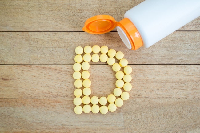 Vitamin D Facts Represented by Tablets Spilling From Bottle to Form Lettter D | Vitacost.com/blog