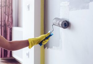 Yellow-Gloved Hand Painting Wall With Roller to Represent Hazardous Chemicals Being Avoided in Home Decorating | Vitacost.com/blog