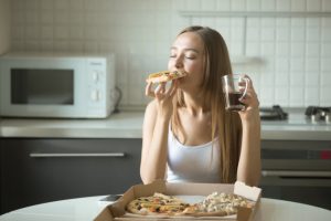 Woman Who Isn't Following a Healthy Vegetarian Diet Savoring a Slice of Pizza With Eyes Closed at Table | Vitacost.com/blog