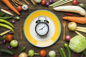Alarm Clock on Pate Surrounded by Fresh Produce to Represent Concepts of Meal Timing and Overnight Fasting | Vitacost.com/blog
