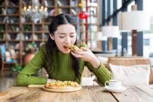 Woman Practicing Mindful Eating Tips Eating Slowly Enjoying Pizza Lunch at Table | Vitacost.com/blog
