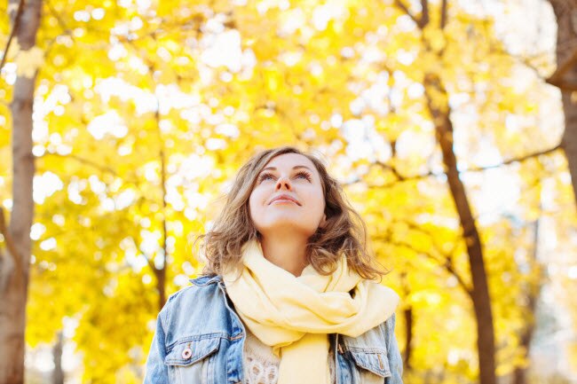 Woman Strolling Through Forest With Yellow Leaves on Trees Following Autumn Healthy Living Tips | Vitacost.com/blog