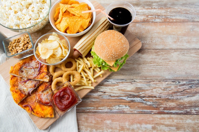 Addictive Junk Food Such as Chips, Fries, Soda and Burgers on Arranged on Wooden Cutting Board | Vitacost.com/blog