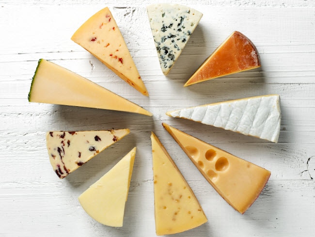 Assorted Wedges of Cheese Arranged in Circle on White Board to Represent Benefits of Dairy | Vitacost.com/blog