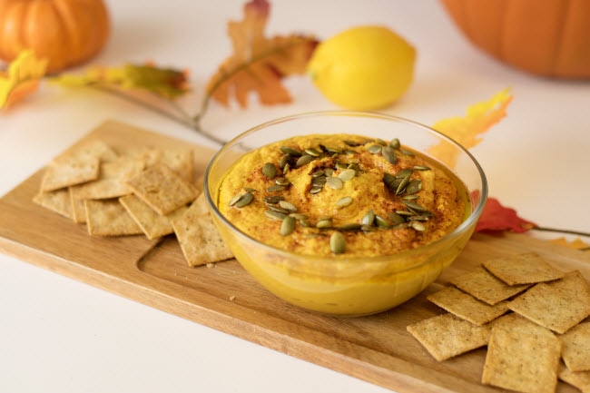 Bowl of Homemade Pumpkin Hummus on Cutting Board with Scattered Crackers and Fall Decorations | Vitacost.com/blog